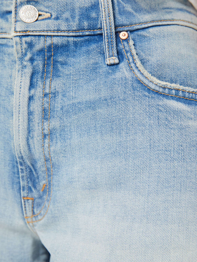 Swatch view of a woman in light blue denim shorts designed to sit lower on the hips with a frayed hem and whiskering, fading, and distressed details. 