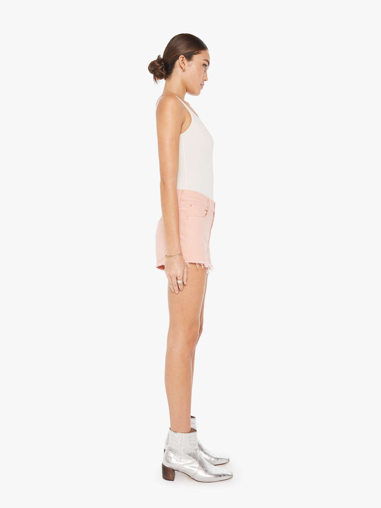 Side view of a faded pink denim short featuring a relaxed mid rise and a short frayed hem.