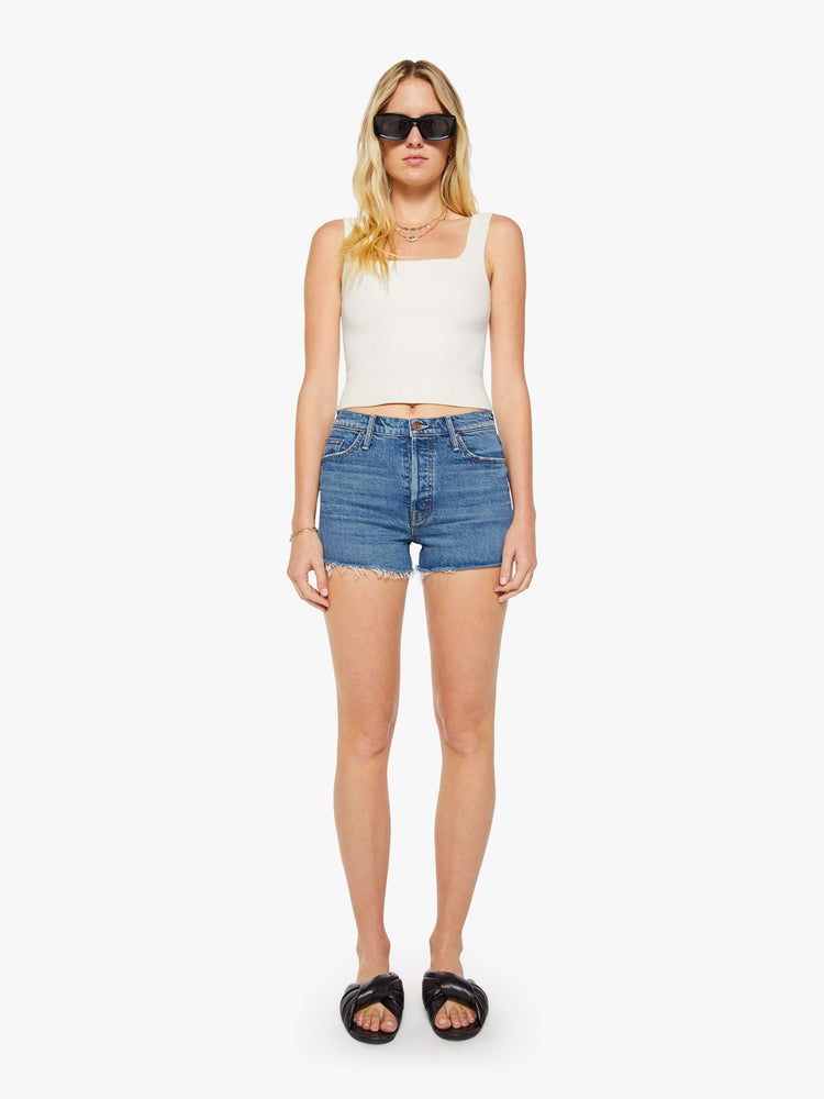 Front view of a woman in a mid blue high-waisted jean shorts with a button fly, 3-inch inseam and a frayed hem.