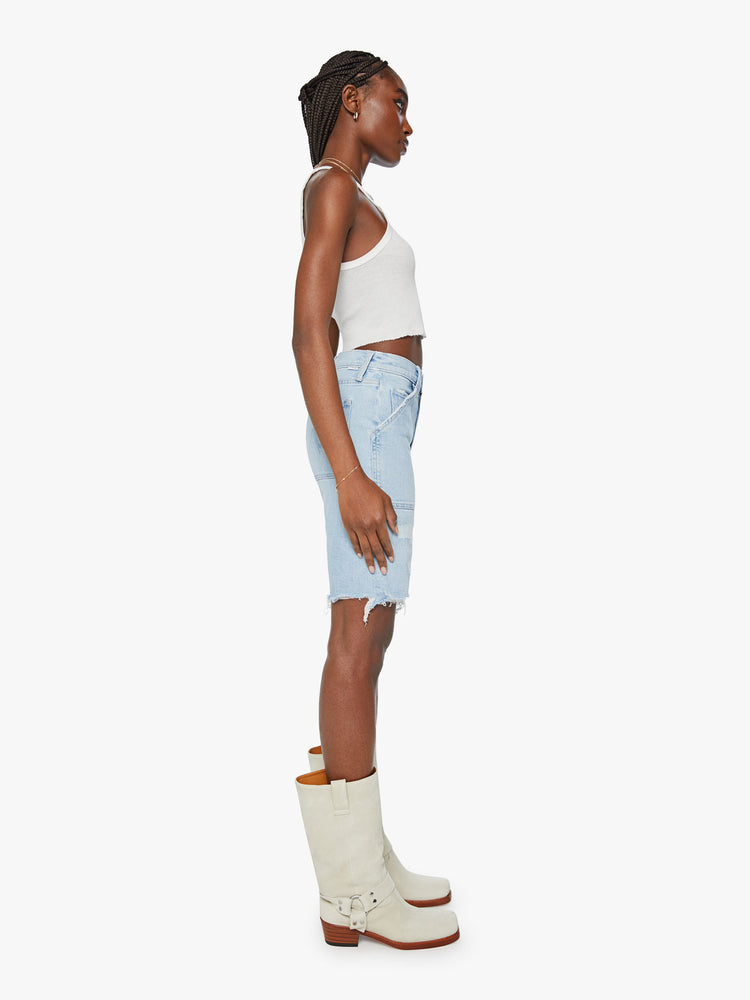 Side view of a woman light blue bermuda shorts with a high rise, oversized patch pockets, a 9-inch inseam and a raw hem.