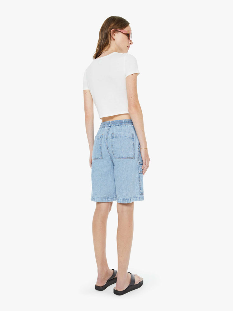 Back view of a woman in a light blue wide-leg denim bermuda shorts with an elastic drawstring waist, oversized patch pockets and a relaxed, low-slung fit. 