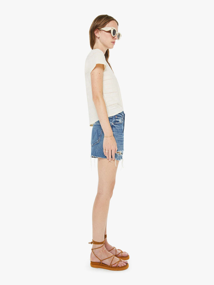 Side view of a woman in a mid blue lived in high-waisted denim shorts with a button fly, 4" inseam and a raw, chewed hem.