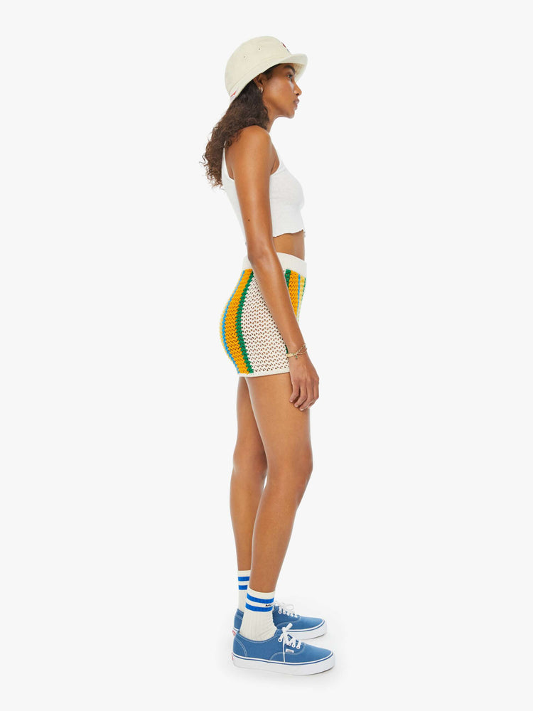 Side view of a woman in cream, orange, green and blue striped crochet shorts featuring delicate openwork details.