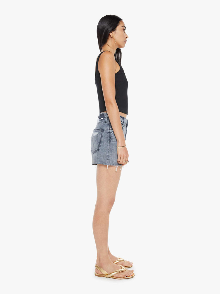 Side view of a woman in a light grey high-waisted denim shorts with a button fly, frayed hem and vintage-inspired fit.