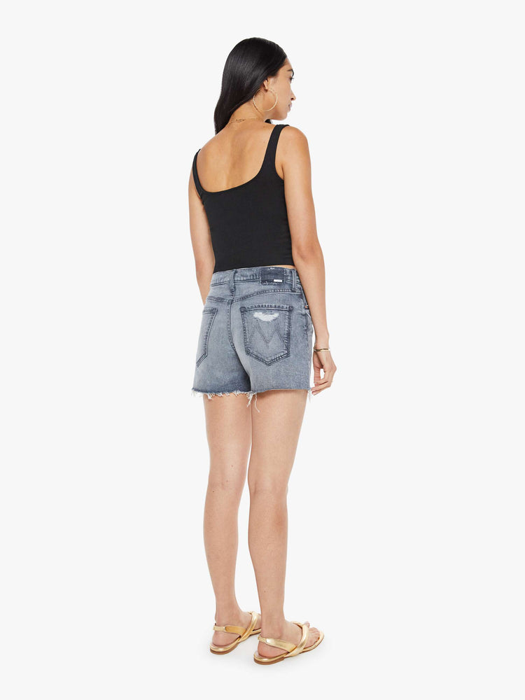 Back view of a woman in a light grey high-waisted denim shorts with a button fly, frayed hem and vintage-inspired fit.