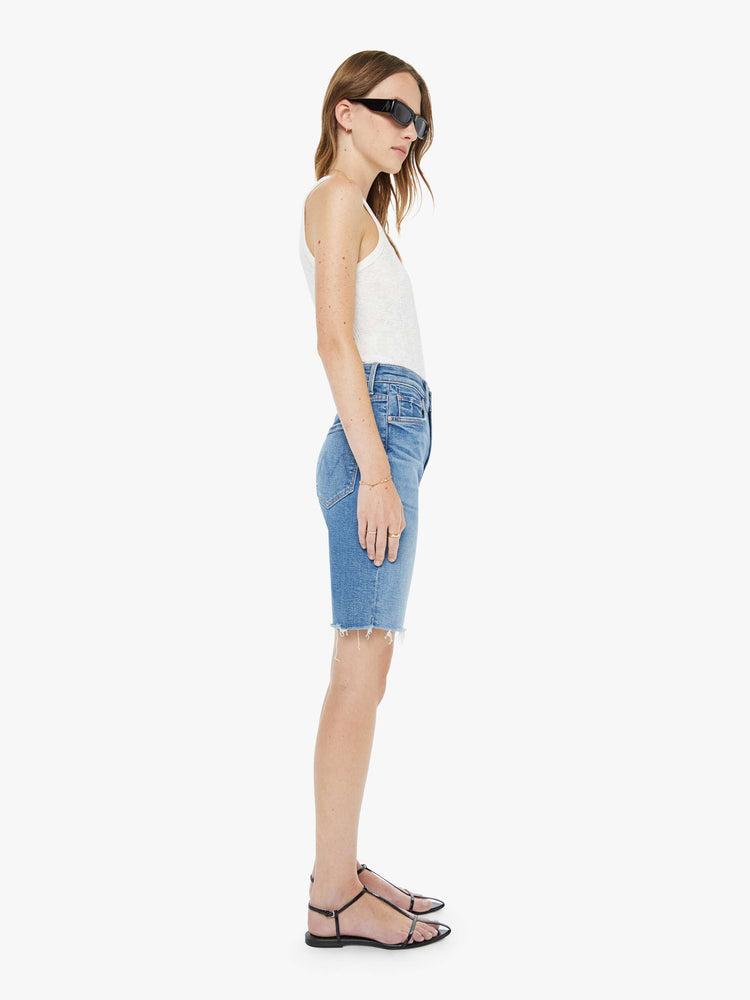 Side view of a woman in a high-waisted denim shorts with a straight leg, zip fly, 9-inch inseam and a frayed hem.