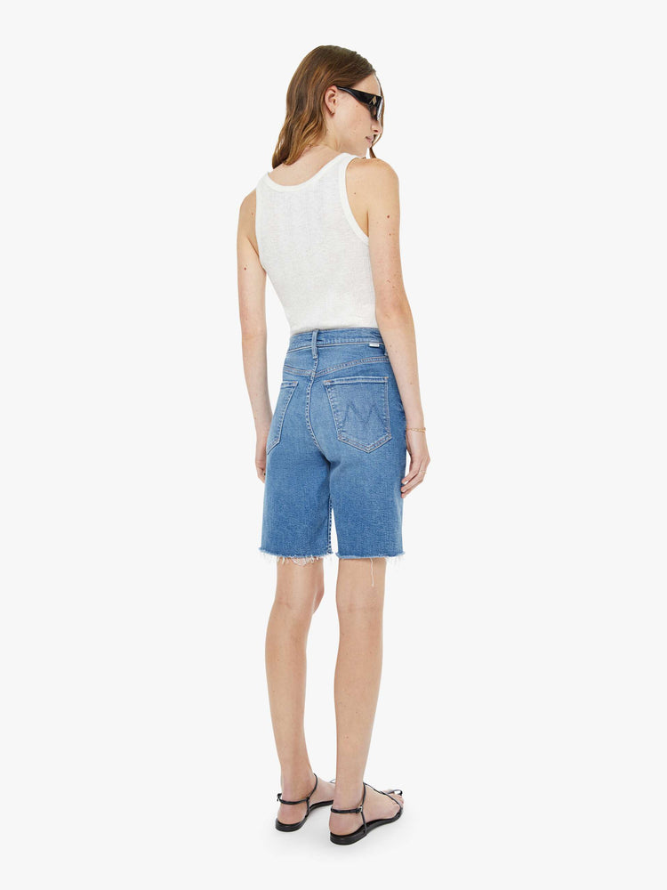 Back view of a woman in a high-waisted denim shorts with a straight leg, zip fly, 9-inch inseam and a frayed hem.