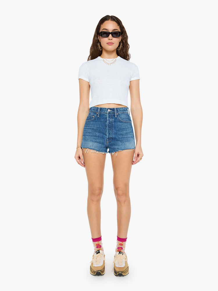 Front view of a woman in a super high-waisted denim shorts with a button fly, 2-inch inseam and a frayed hem in mid blue wash with cherries embroidered.