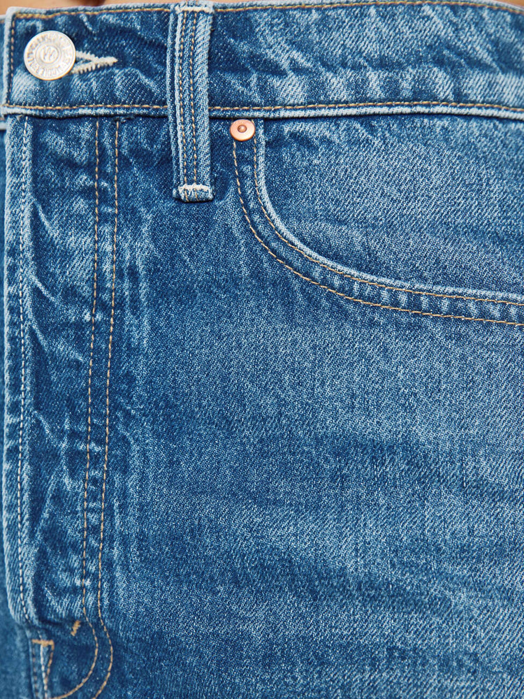 Close up view of a woman in a super high-waisted denim shorts with a button fly, 2-inch inseam and a frayed hem in mid blue wash with cherries embroidered.