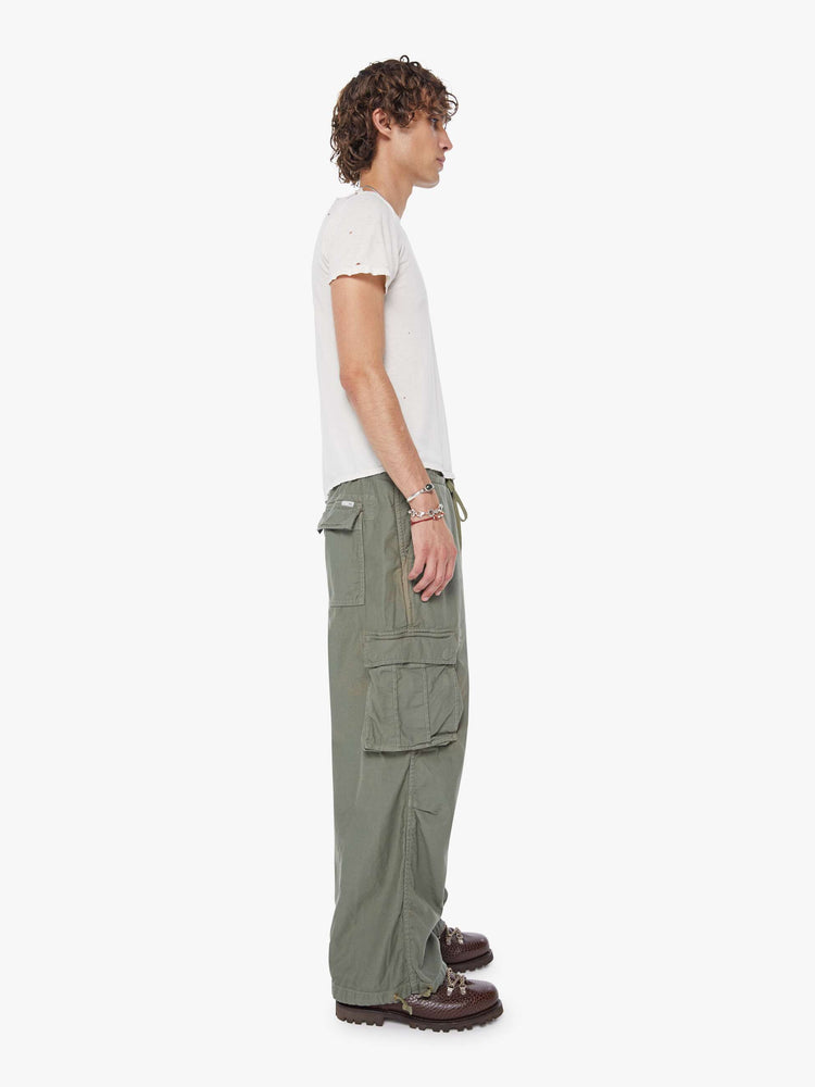 Side  view of a man in an army green military-inspired pants with a loose leg, slightly dropped crotch, oversized cargo pockets, a 26.5-inch inseam and drawstring hems.