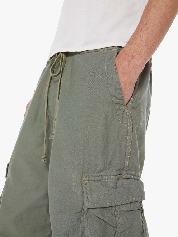 Close up  view of a man in an army green military-inspired pants with a loose leg, slightly dropped crotch, oversized cargo pockets, a 26.5-inch inseam and drawstring hems.