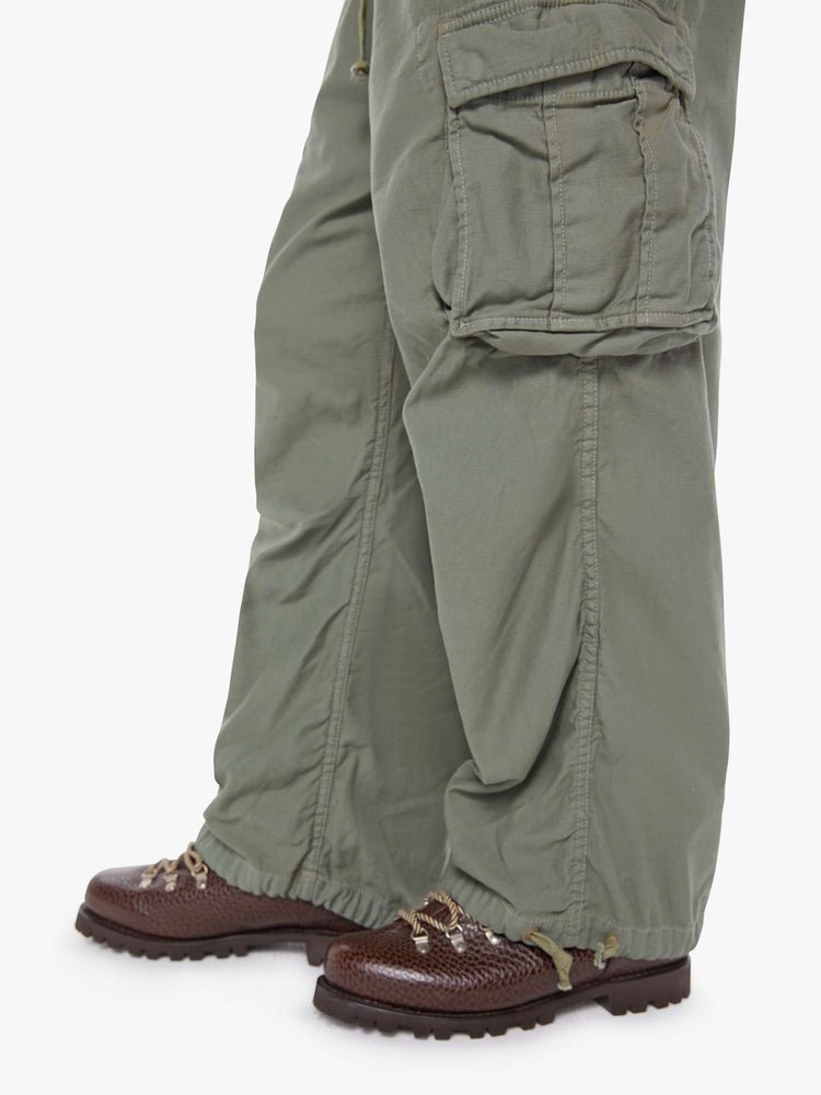 Hem close up  view of a man in an army green military-inspired pants with a loose leg, slightly dropped crotch, oversized cargo pockets, a 26.5-inch inseam and drawstring hems.
