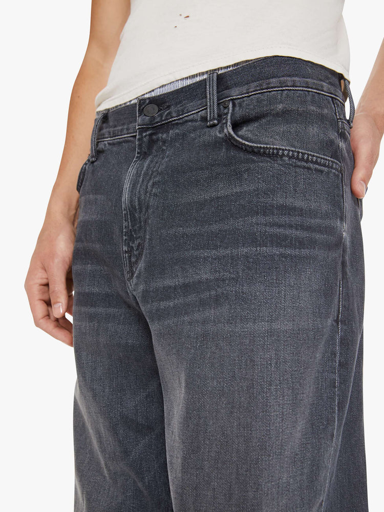 Close up view of a man in faded black loose-fitting jean with a mid rise, zip fly, 31-inch inseam and a clean hem.