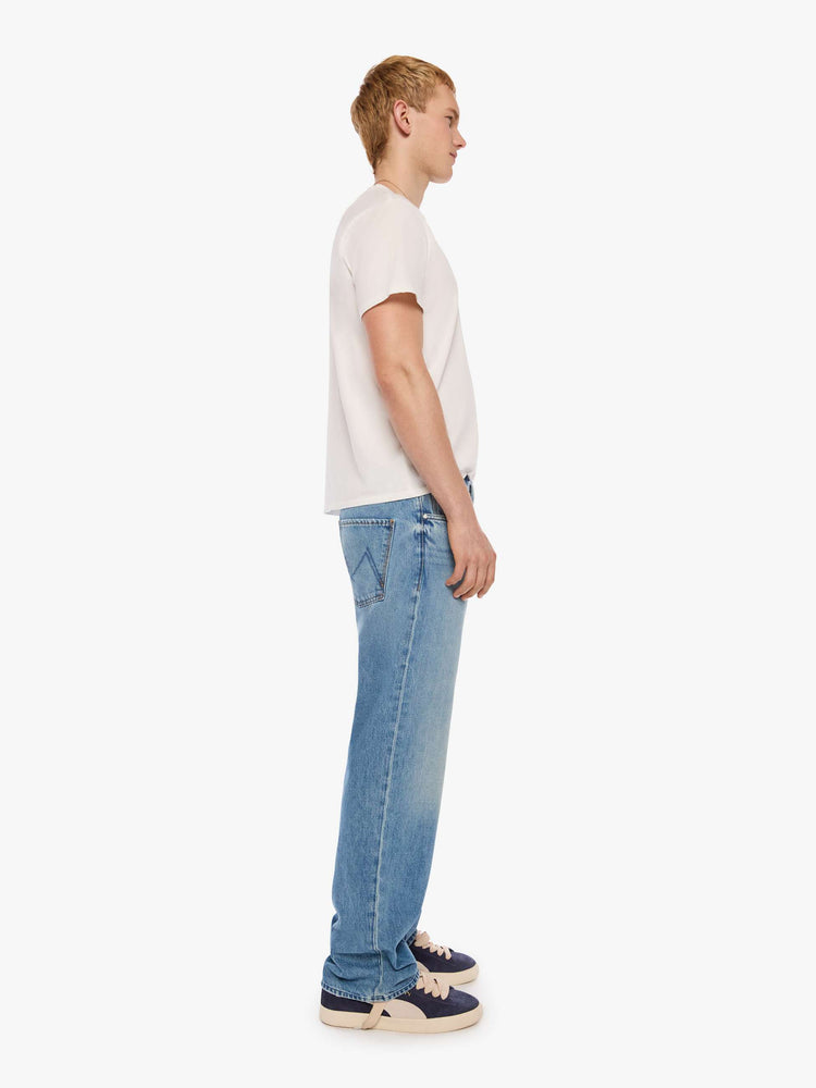 Side view of a man in light blue loose-fitting jean with a mid rise, zip fly, 31-inch inseam and a clean hem.