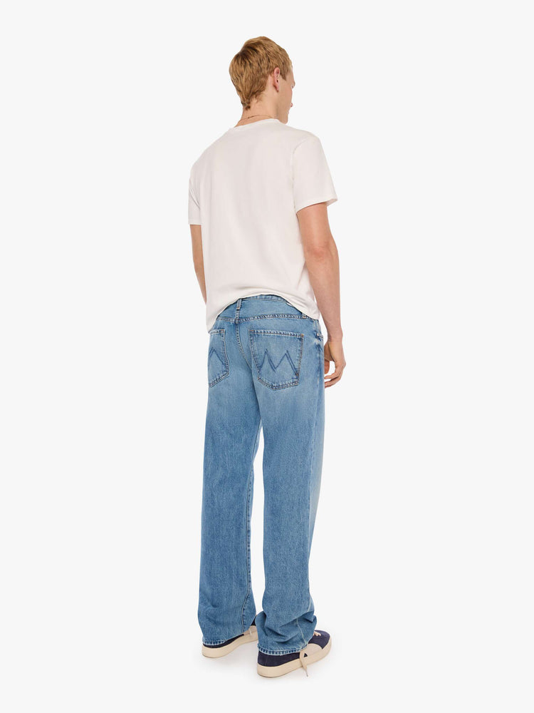 Back view of a man in light blue loose-fitting jean with a mid rise, zip fly, 31-inch inseam and a clean hem.