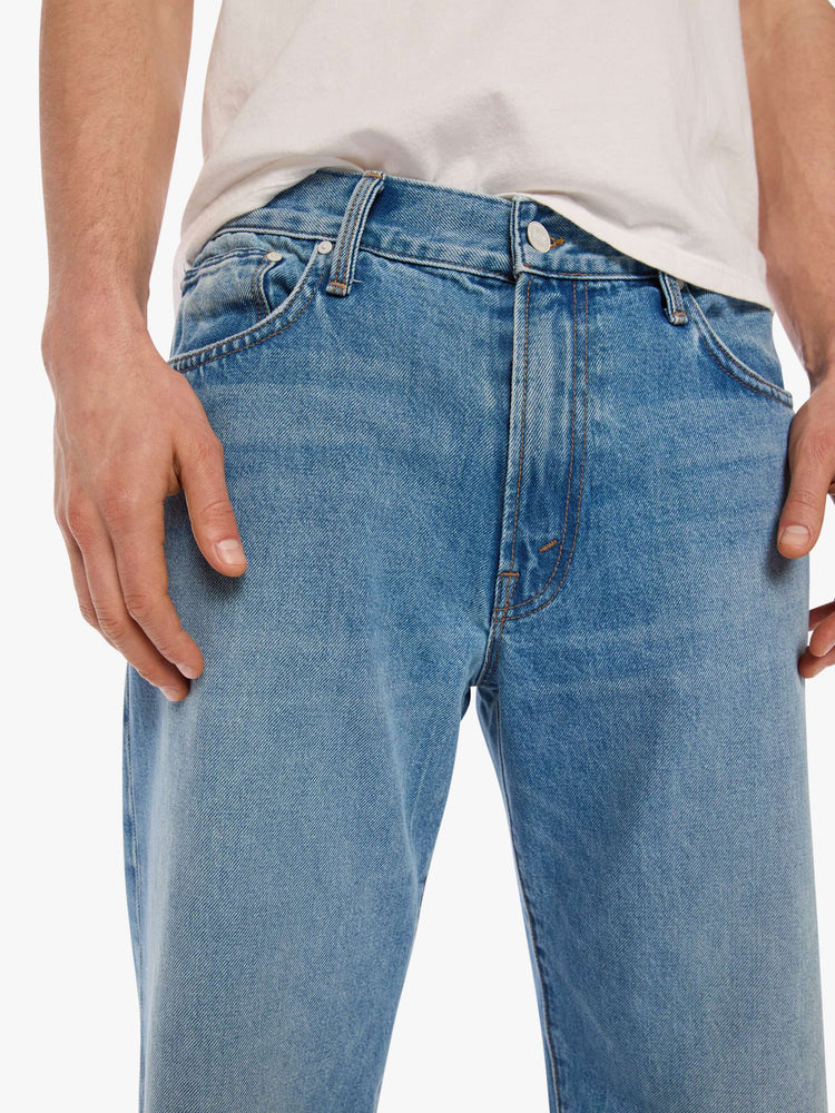 Clos up view of a man in light blue loose-fitting jean with a mid rise, zip fly, 31-inch inseam and a clean hem.