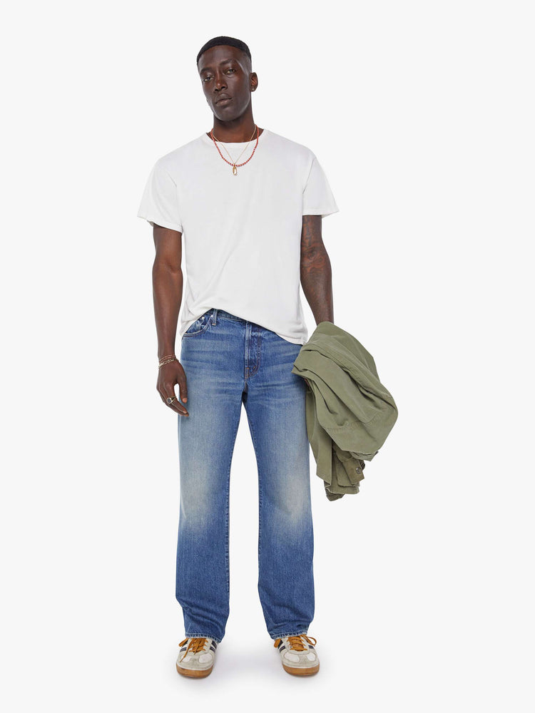 Front view of a man in a mid-blue loose-fitting jean with a mid rise, zip fly, 31-inch inseam and a clean hem.