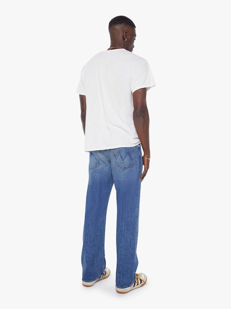 Back view of a man in a mid-blue loose-fitting jean with a mid rise, zip fly, 31-inch inseam and a clean hem.