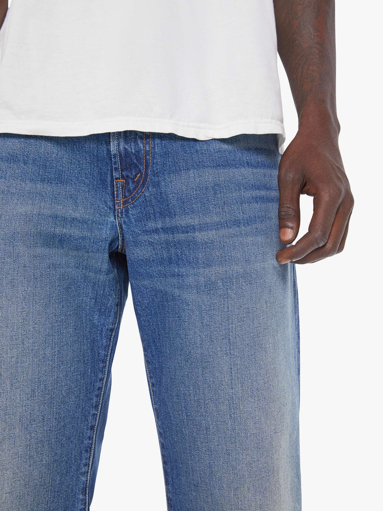 Close up view of a man in a mid-blue loose-fitting jean with a mid rise, zip fly, 31-inch inseam and a clean hem.