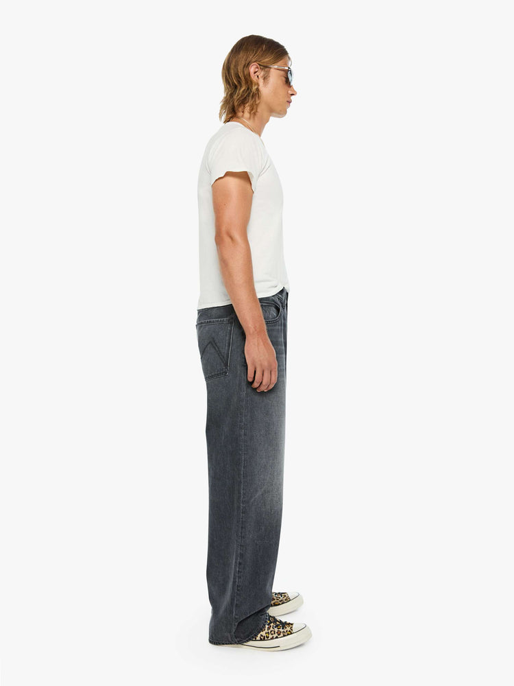 Side view of a man in dark grey baggy jean with a high rise, zip fly, 30-inch inseam and a clean hem.