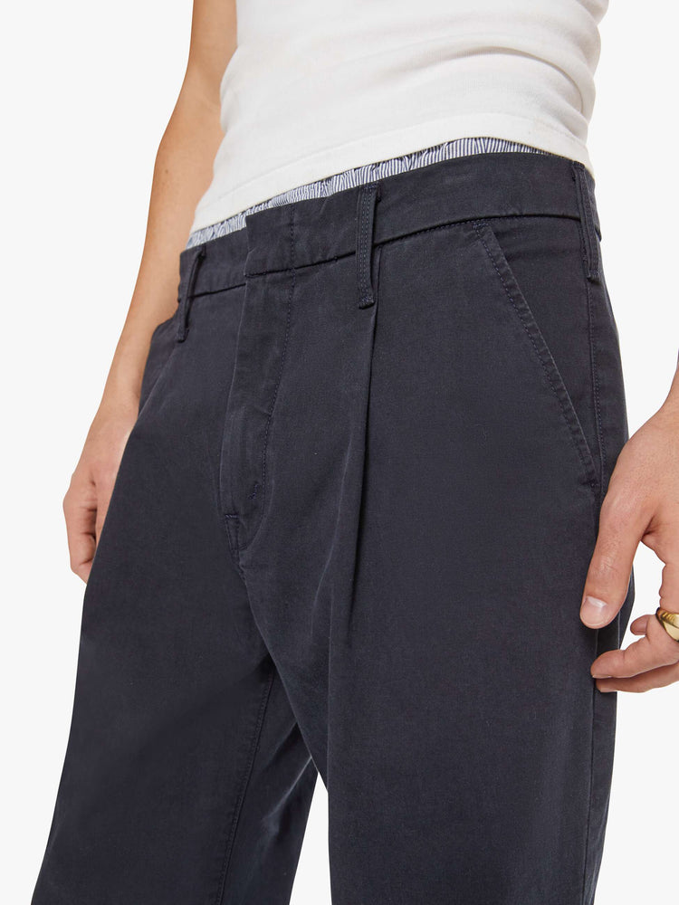 Close up view of a man in a navy relaxed pants with a mid rise, pleats at the waistband, a zip fly, slit pockets and a 31-inch inseam with a clean hem.