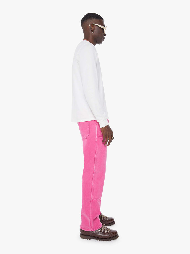 Side view of a man in hot pink loose-fitting jean with a mid rise, zip fly, hammer loop, 31-inch inseam and a clean hem.