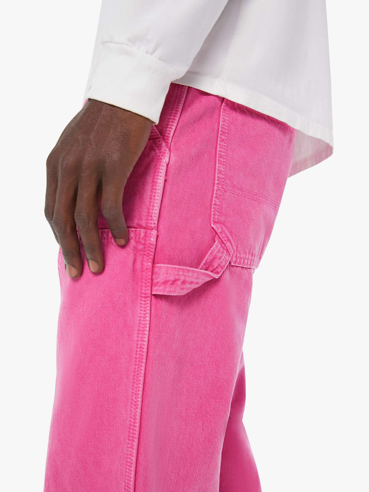 Close up view of a man in hot pink loose-fitting jean with a mid rise, zip fly, hammer loop, 31-inch inseam and a clean hem.