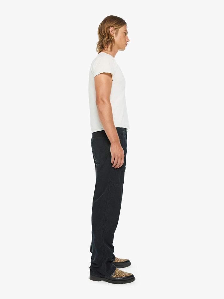 Side  view of a man in a corduroy pant with a loose straight leg, patch pockets, a zipper pocket along the outer seam, patches on the knees, a hammer loop, zip fly and a 32-inch inseam with a clean hem.