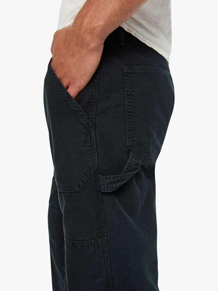 Close up  view of a man in a corduroy pant with a loose straight leg, patch pockets, a zipper pocket along the outer seam, patches on the knees, a hammer loop, zip fly and a 32-inch inseam with a clean hem.