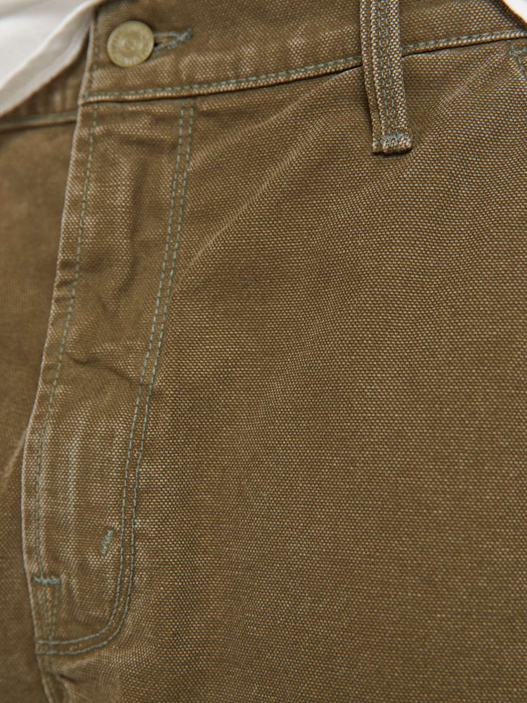 Swatch view of a man in a dark olive mid-rise shorts with a zip fly, slit pockets, a hammer loop, utility-inspired patches at the knees and a raw, cut-off hem.