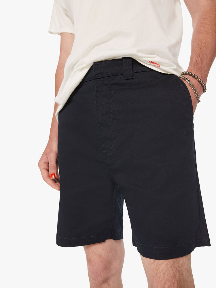 Close up view of men jean short with a straight leg, slash pockets and an inseam above the knee in a dark navy hue.