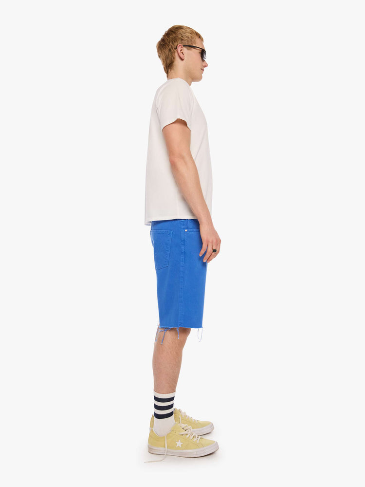 Side view of a man in a bright primary  blue loose-fitting jean short with a mid rise, zip fly, knee-length inseam and a clean hem.