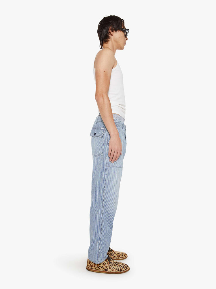 Side view of a man in light blue pin stripe high-waisted jeans designed to sit lower on the hips with a slightly tapered leg, button fly, oversized patch pockets and a loose fit.