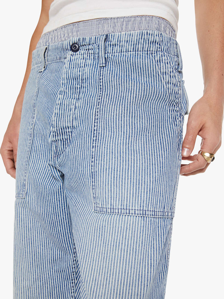 Close up view of a man in light blue pin stripe high-waisted jeans designed to sit lower on the hips with a slightly tapered leg, button fly, oversized patch pockets and a loose fit.