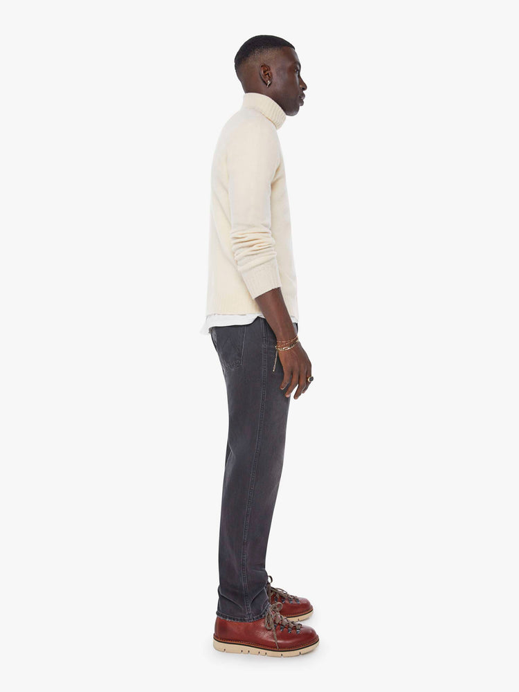 Side view of a man in a dark grey straight-leg jean with a mid rise, zip fly, 30-inch inseam and a clean hem. 