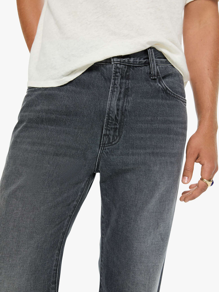 Close up view of a man in a dark grey straight-leg jean with a mid rise, zip fly, 31-inch inseam and a clean hem.