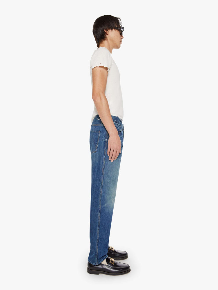Side view of a man in a med blue straight-leg jean with a mid rise, zip fly, 31-inch inseam and a clean hem.