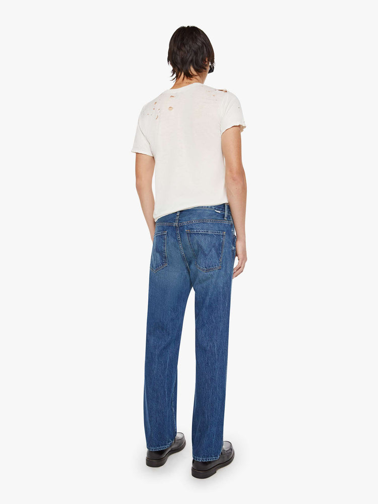 Back view of a man in a med blue straight-leg jean with a mid rise, zip fly, 31-inch inseam and a clean hem.