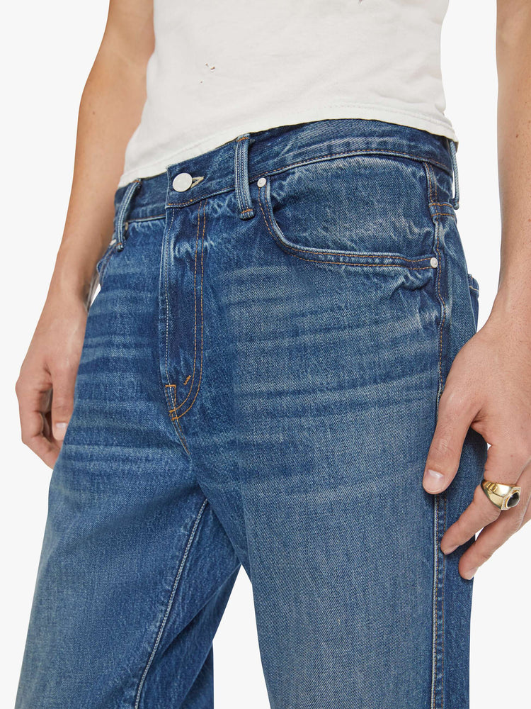 Close up view of a man in a med blue straight-leg jean with a mid rise, zip fly, 31-inch inseam and a clean hem.