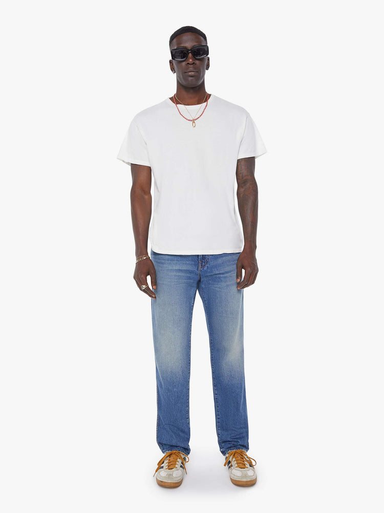 Front view of a man in a mid blue  straight-leg jean with a mid rise, zip fly, 30-inch inseam and a clean hem. 