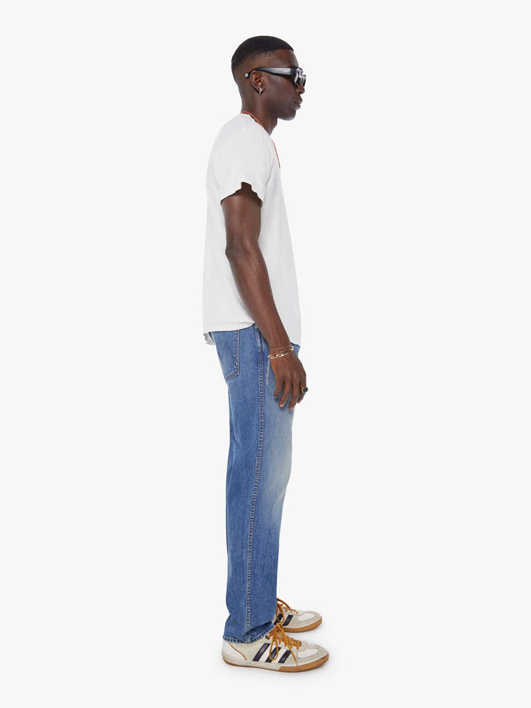 Side view of a man in a mid blue  straight-leg jean with a mid rise, zip fly, 30-inch inseam and a clean hem. 