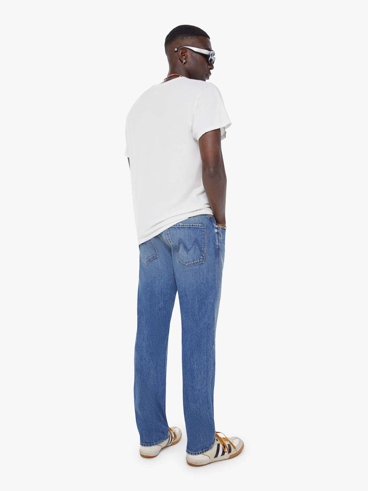 Back view of a man in a mid blue  straight-leg jean with a mid rise, zip fly, 30-inch inseam and a clean hem. 