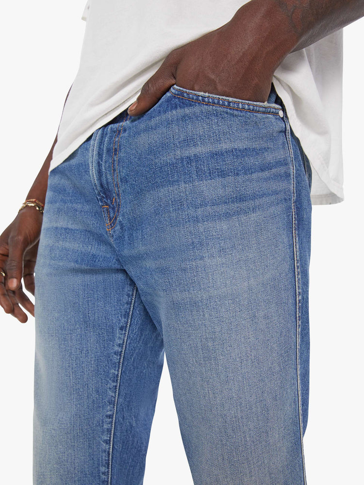 Close up view of a man in a mid blue  straight-leg jean with a mid rise, zip fly, 30-inch inseam and a clean hem. 