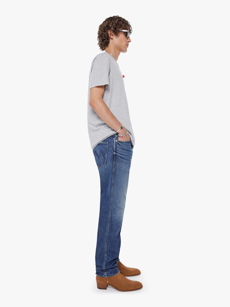 Side view of a man in a mid-blue straight-leg jean with a mid rise, zip fly, 30-inch inseam and a clean hem.