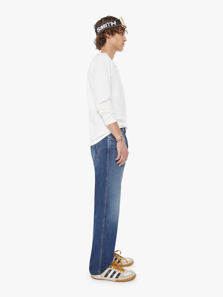 Side view of a woman in a med blue straight-leg jean with a mid rise, zip fly, 30-inch inseam and a clean hem.