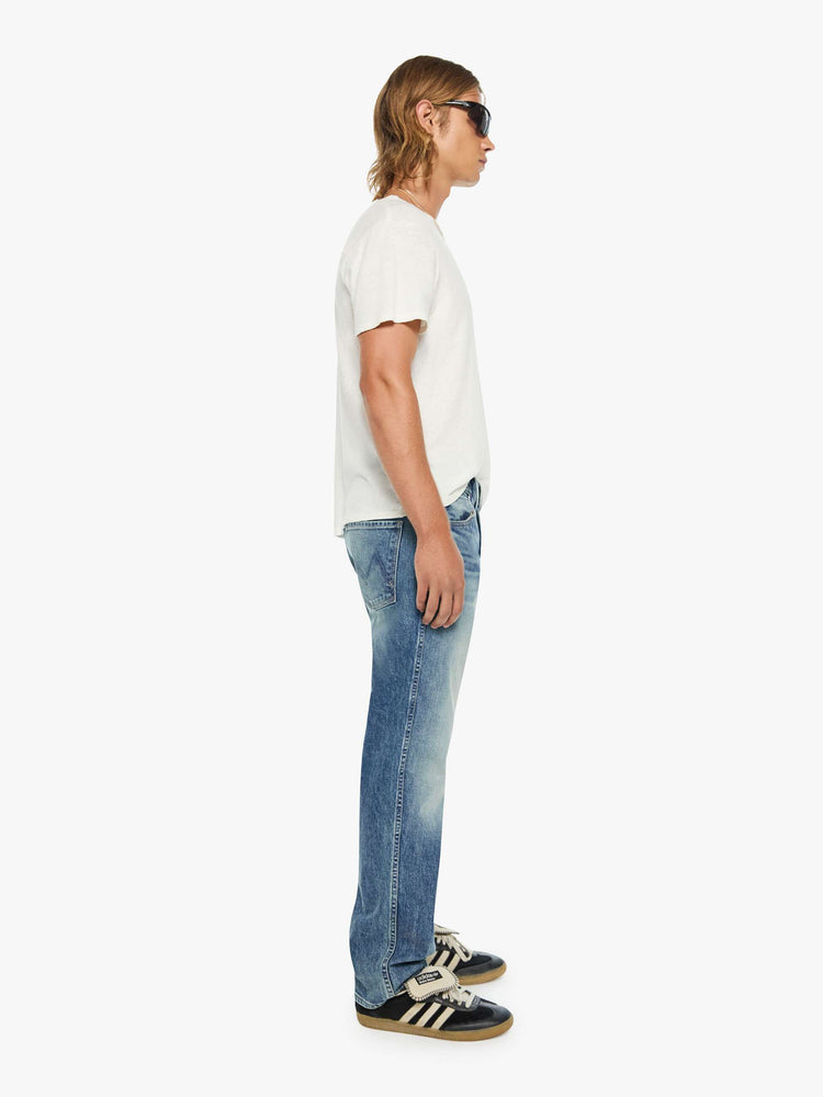 Side view of a man in a mid blue  straight-leg jean with a mid rise, zip fly, 31-inch inseam and a clean hem.