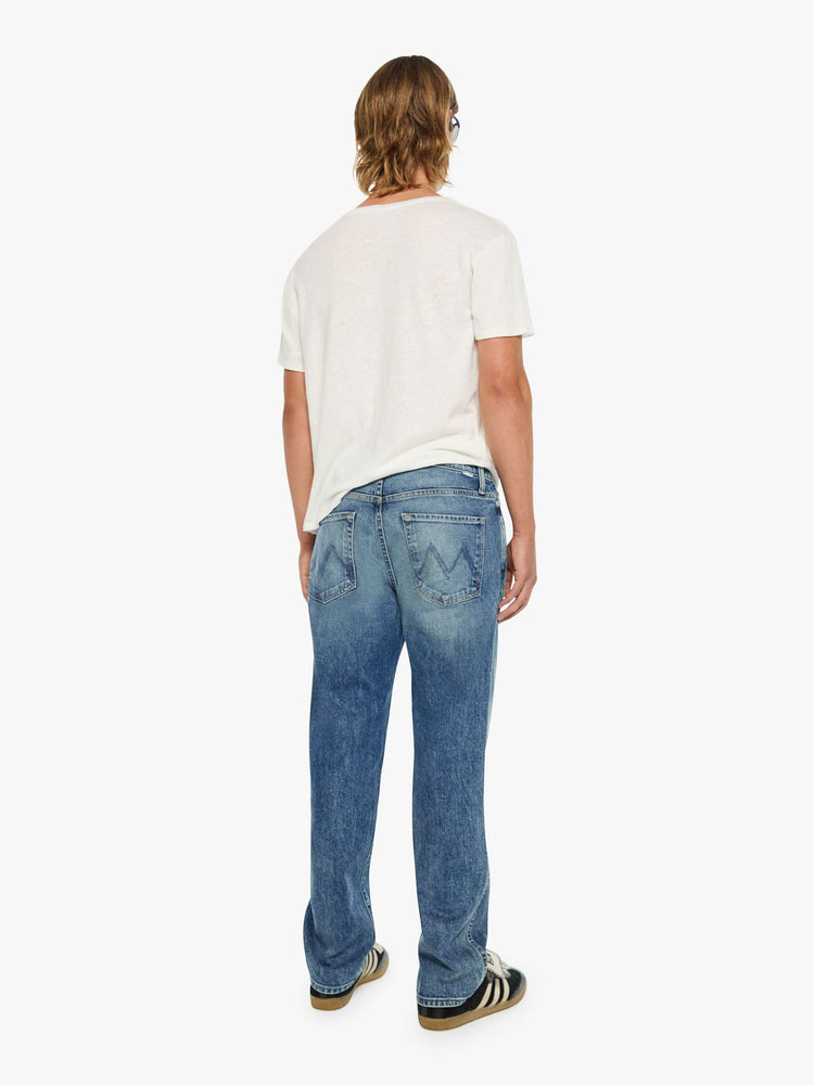 Back view of a man in a mid blue  straight-leg jean with a mid rise, zip fly, 31-inch inseam and a clean hem.