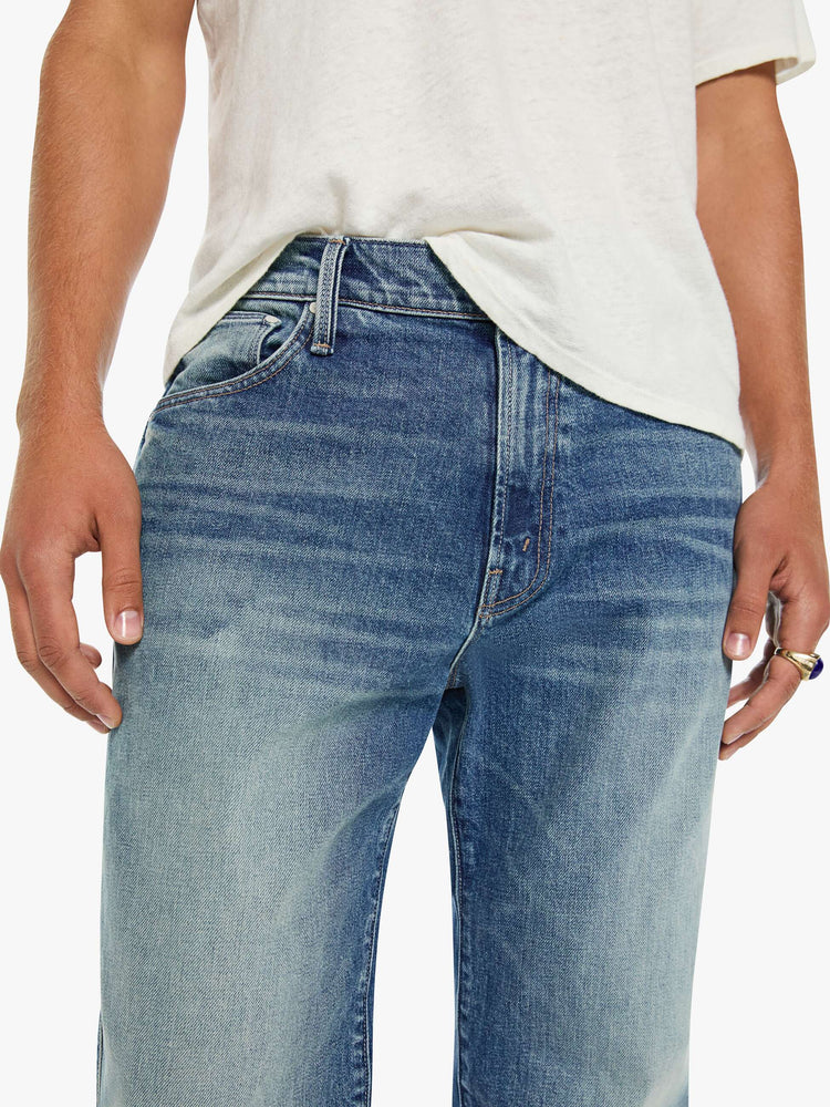 Close up view of a man in a mid blue  straight-leg jean with a mid rise, zip fly, 31-inch inseam and a clean hem.