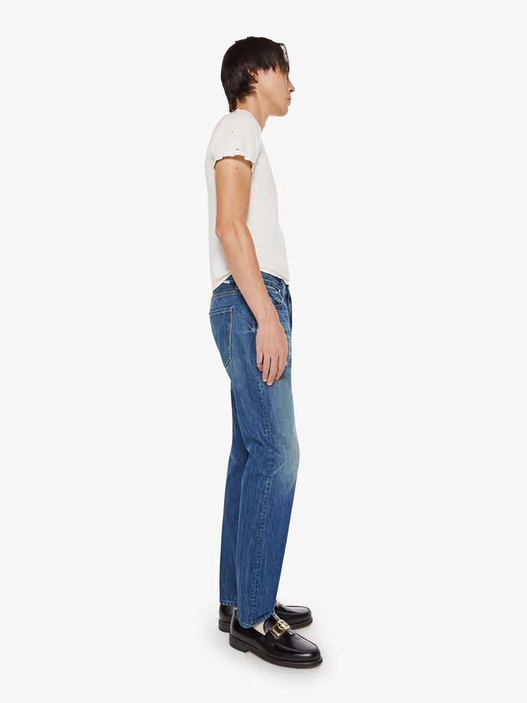 Side view of a man in a mid blue jean with a standard straight leg with a mid rise, button fly and 32-inch inseam with a clean hem.