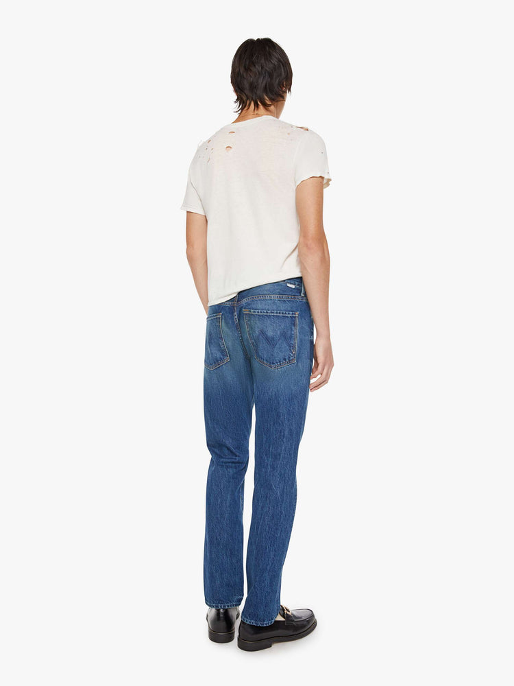 Back view of a man in a mid blue jean with a standard straight leg with a mid rise, button fly and 32-inch inseam with a clean hem.